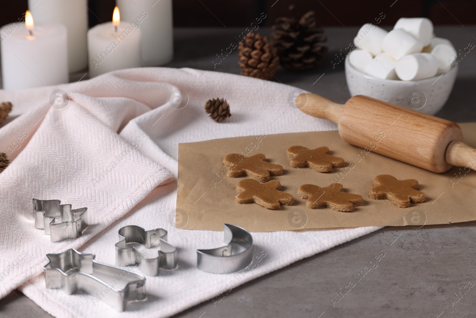 Photo of Uncooked cookies, cutters, pine cones, marshmallows, rolling pin and burning candles on grey table