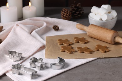 Uncooked cookies, cutters, pine cones, marshmallows, rolling pin and burning candles on grey table