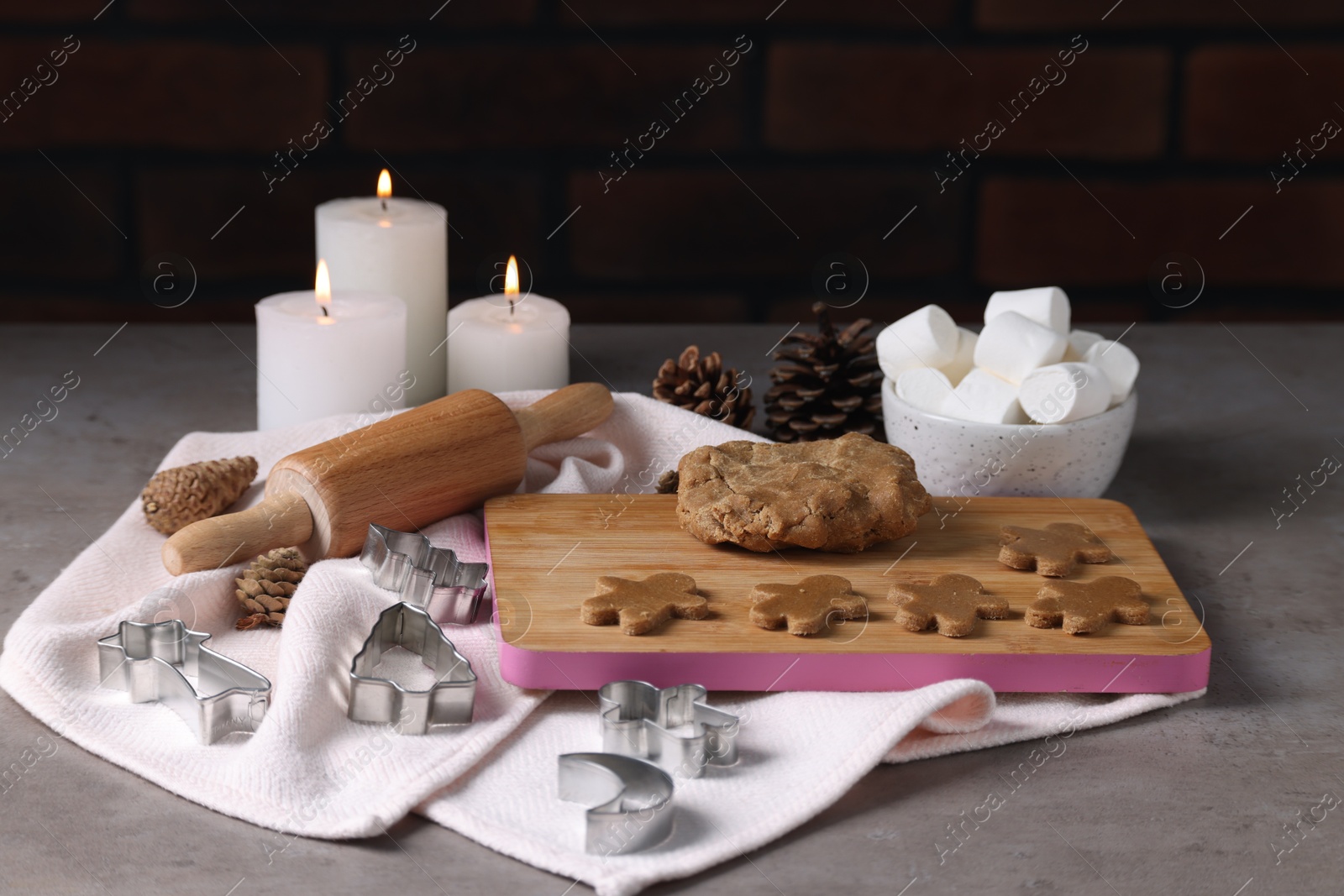 Photo of Raw dough, cookie cutters, pine cones, marshmallows, rolling pin and burning candles on grey table