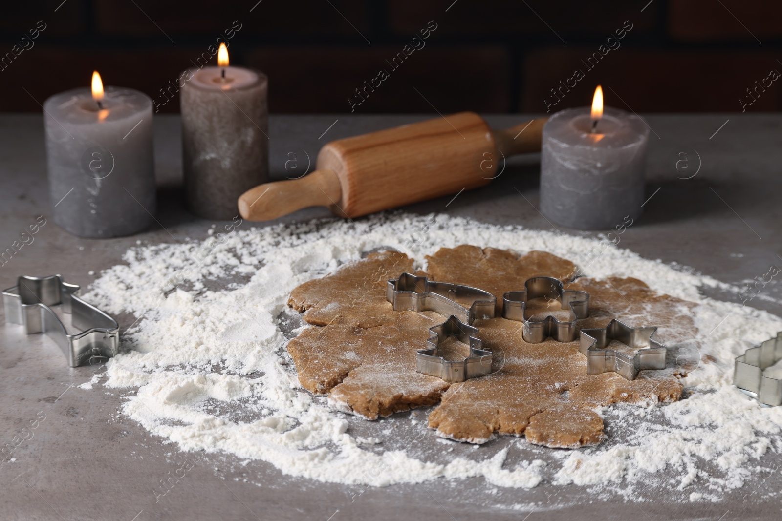 Photo of Raw dough, cookie cutters, rolling pin and burning candles on grey table