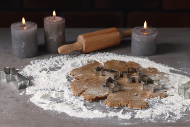 Photo of Raw dough, cookie cutters, rolling pin and burning candles on grey table