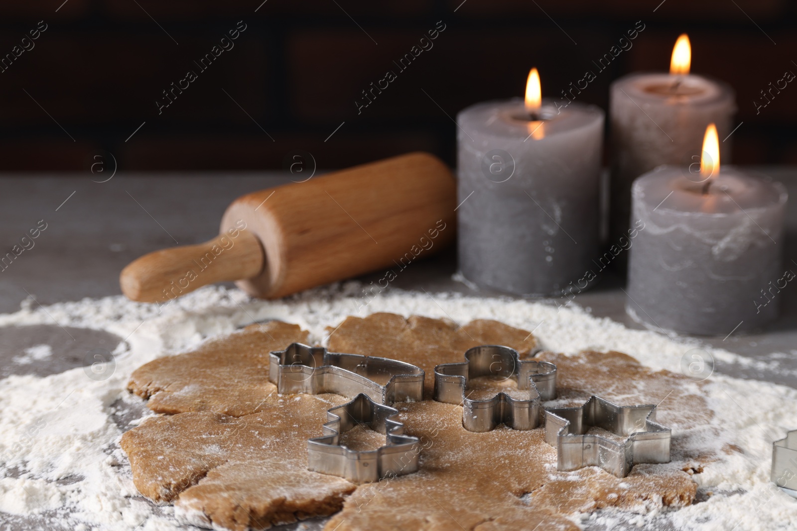 Photo of Raw dough, cookie cutters, rolling pin and burning candles on grey table, closeup