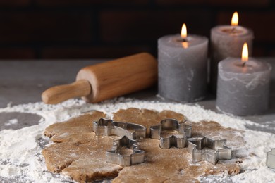 Raw dough, cookie cutters, rolling pin and burning candles on grey table, closeup