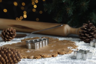 Photo of Raw dough, cookie cutters, pine cones and rolling pin on table, closeup