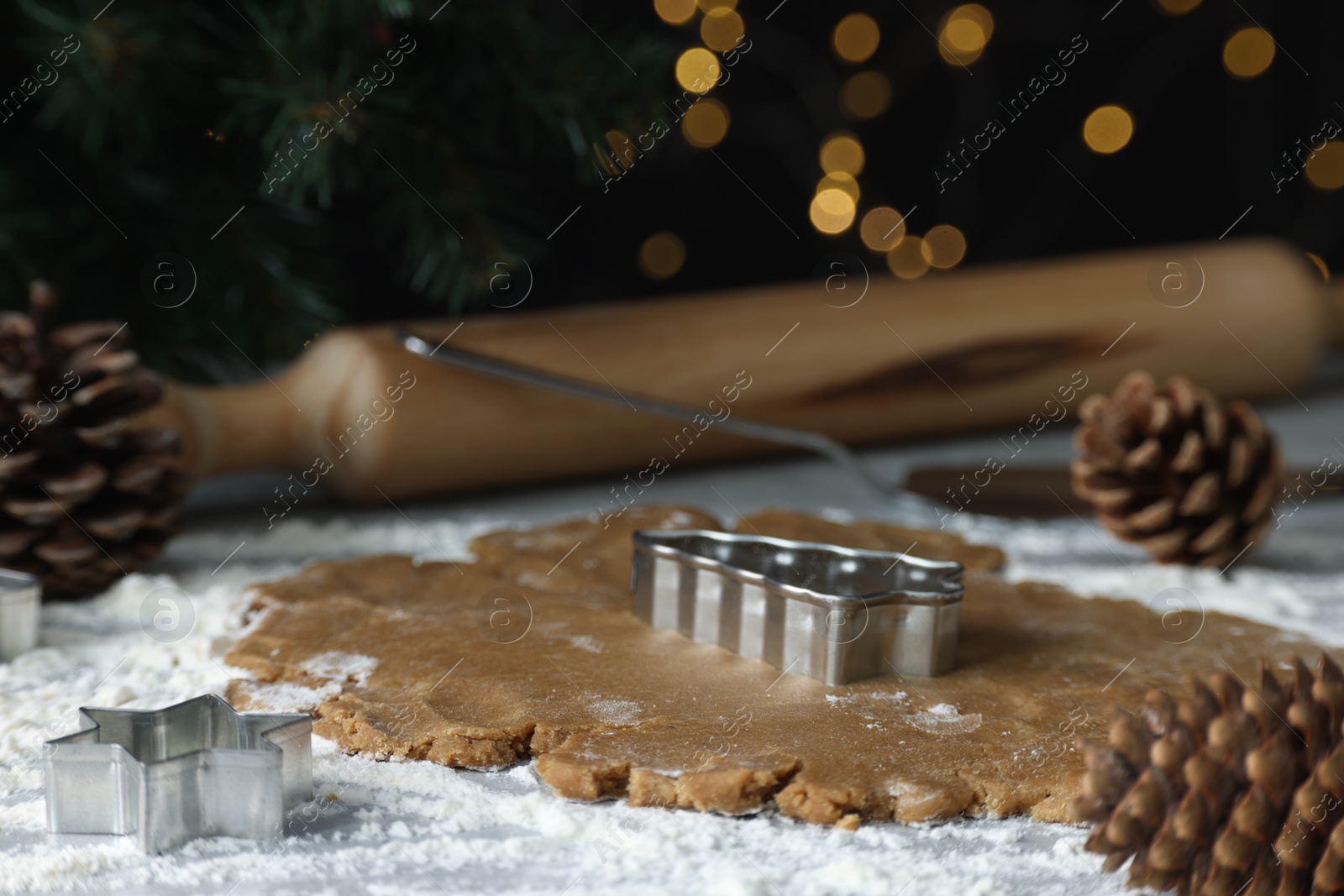 Photo of Raw dough, cookie cutters, pine cones and rolling pin on table, closeup