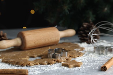 Raw dough, cookie cutters, pine cone, whisk and rolling pin on grey table, closeup