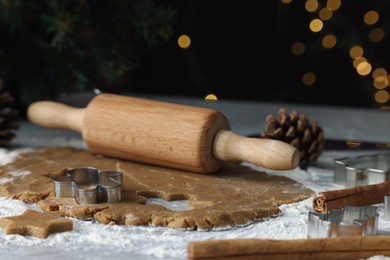 Photo of Raw dough, cookie cutters, pine cone and rolling pin on grey table, closeup