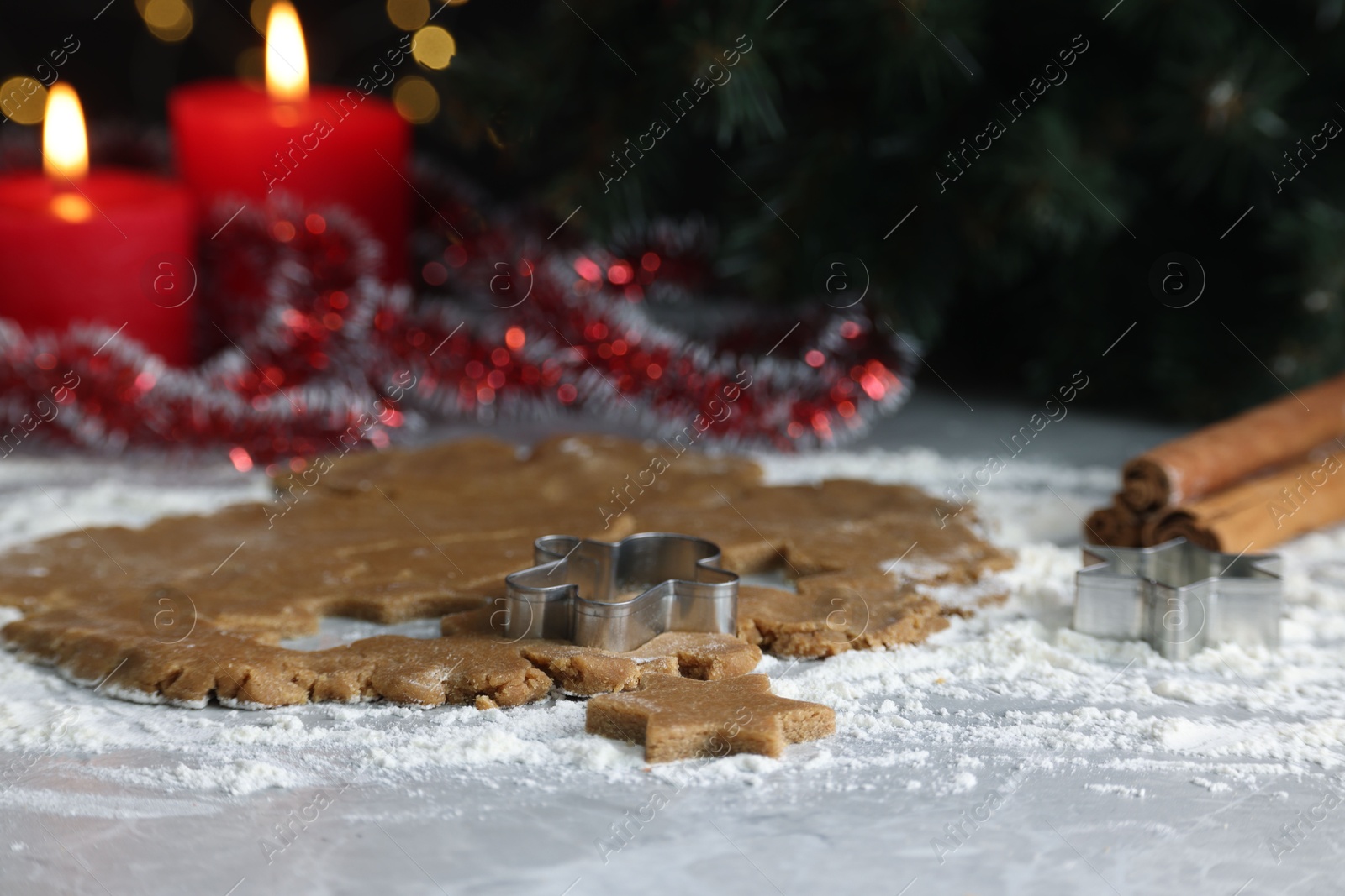 Photo of Raw dough, cookie cutters, cinnamon and burning candles on grey marble table, closeup