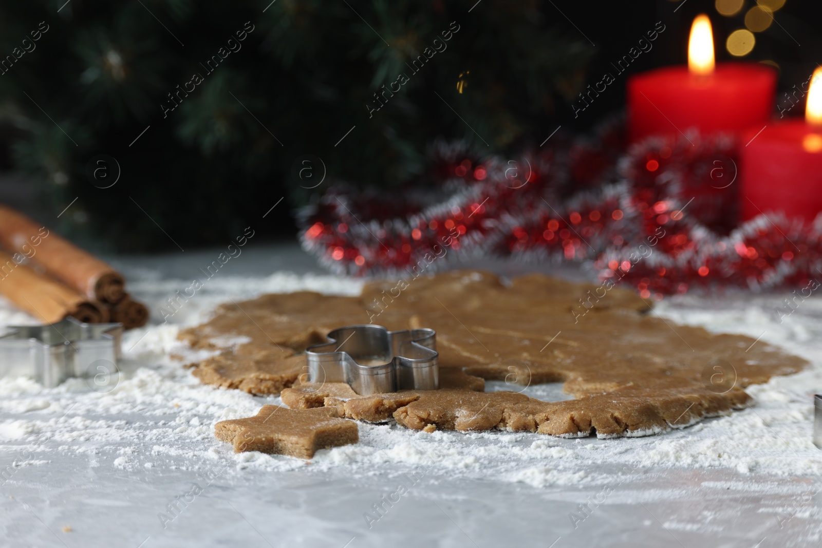 Photo of Raw dough, cookie cutters, cinnamon and burning candles on grey marble table, closeup