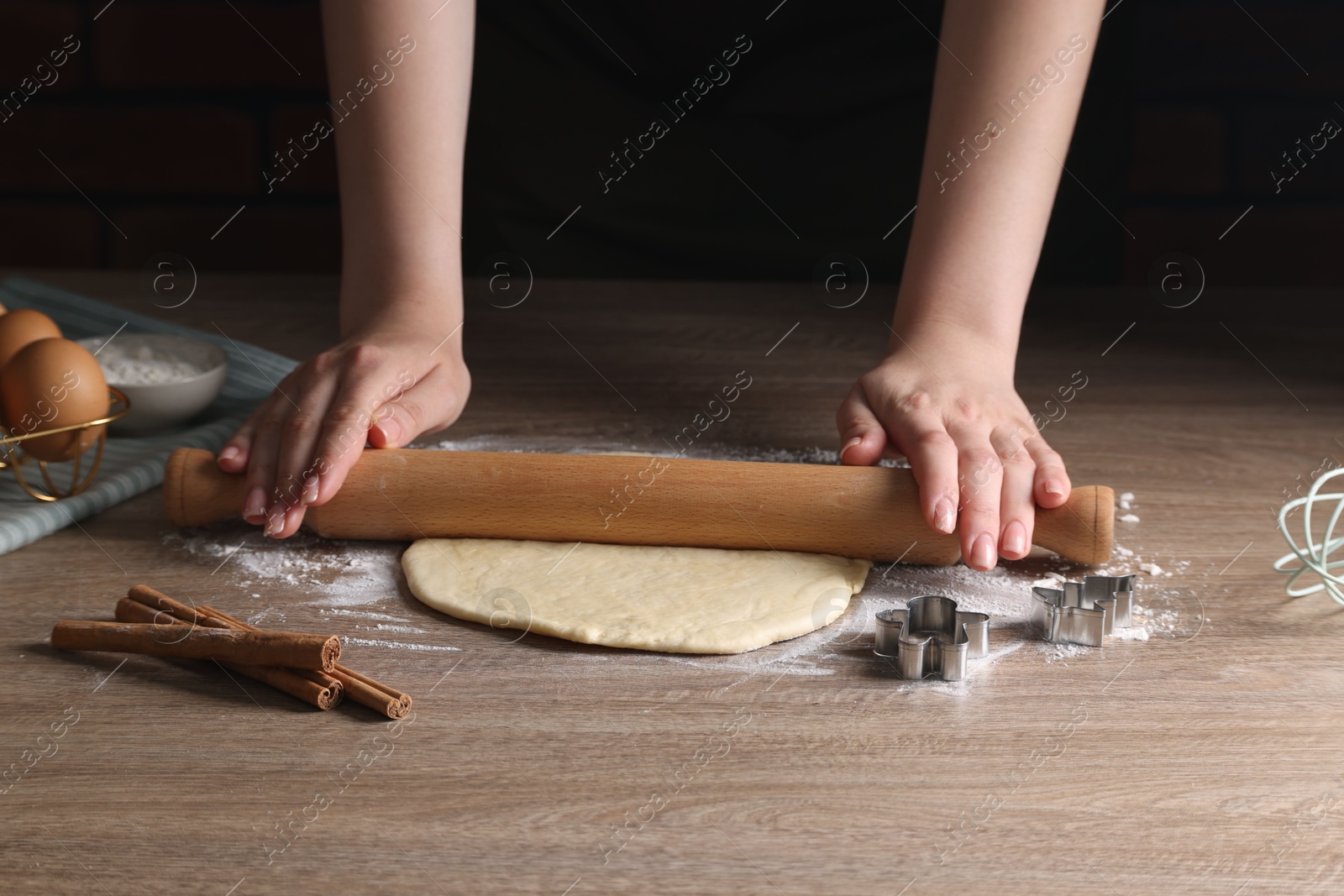 Photo of Woman rolling out dough for cookies at wooden table, closeup