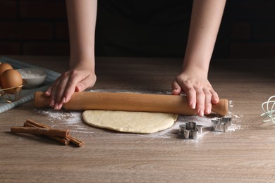 Photo of Woman rolling out dough for cookies at wooden table, closeup