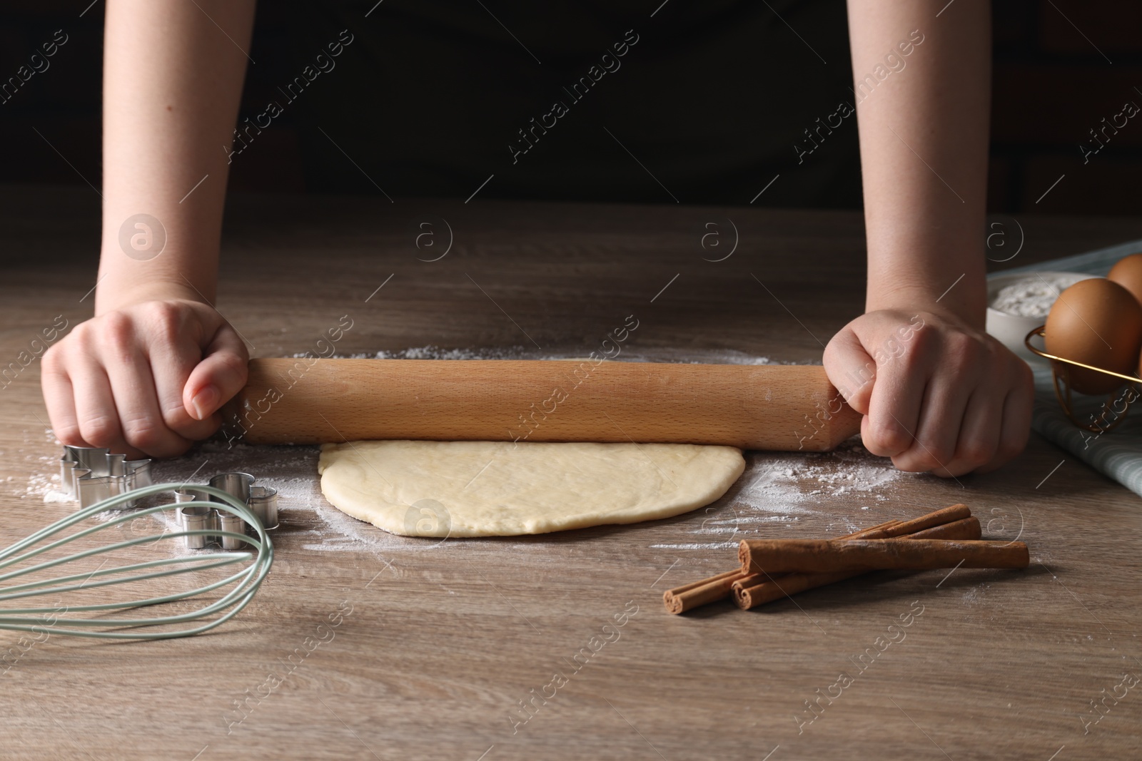 Photo of Woman rolling out dough for cookies at wooden table, closeup