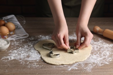 Photo of Woman cutting dough with cookie cutter at wooden table, closeup