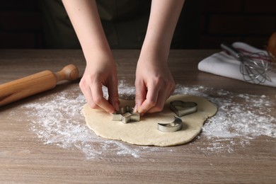 Photo of Woman cutting dough with cookie cutter at wooden table, closeup