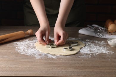 Woman cutting dough with cookie cutter at wooden table, closeup