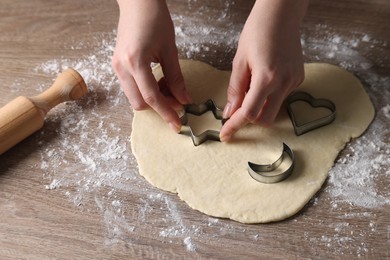 Photo of Woman cutting dough with cookie cutter at wooden table, closeup