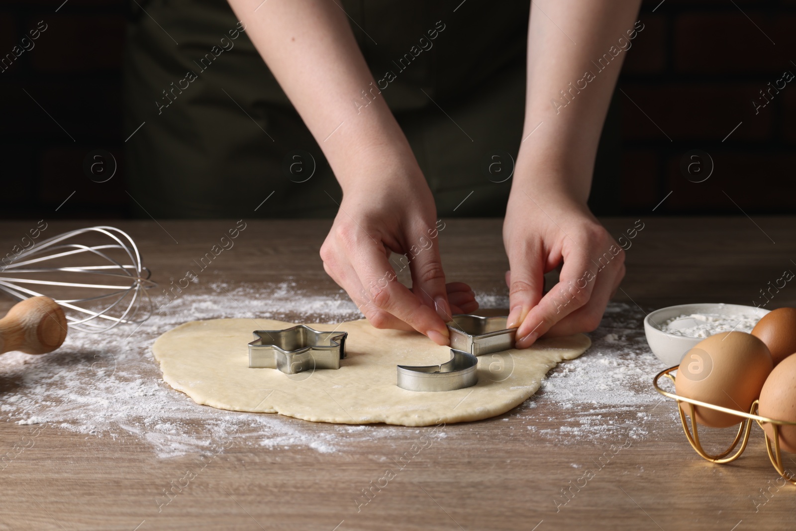 Photo of Woman cutting dough with cookie cutter at wooden table, closeup