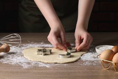 Woman cutting dough with cookie cutter at wooden table, closeup