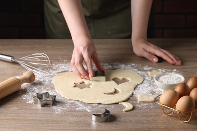 Woman cutting dough with cookie cutter at wooden table, closeup