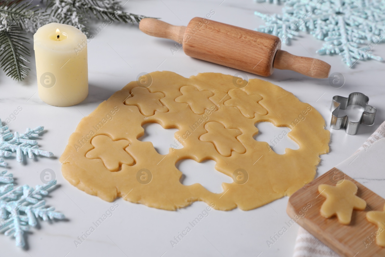 Photo of Making cookies. Raw dough, rolling pin, cutter and burning candle on white marble table