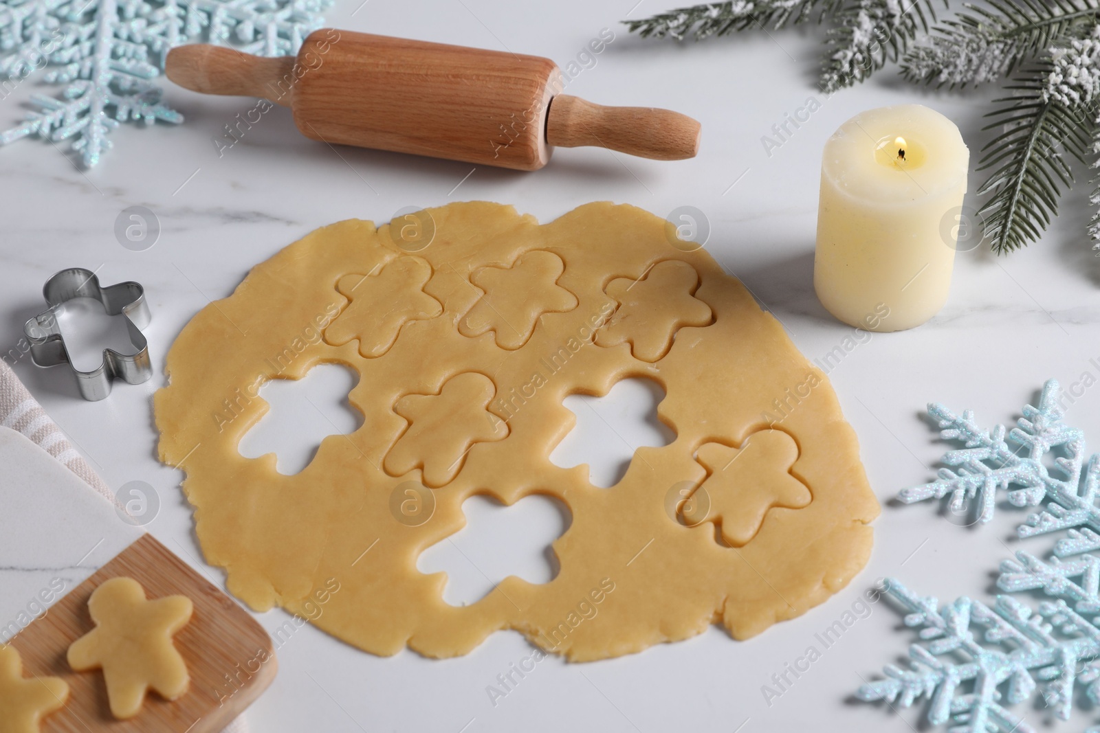 Photo of Making cookies. Raw dough, rolling pin, cutter and burning candle on white marble table