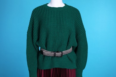 Photo of Female mannequin dressed in dark green sweater with belt and skirt on light blue background