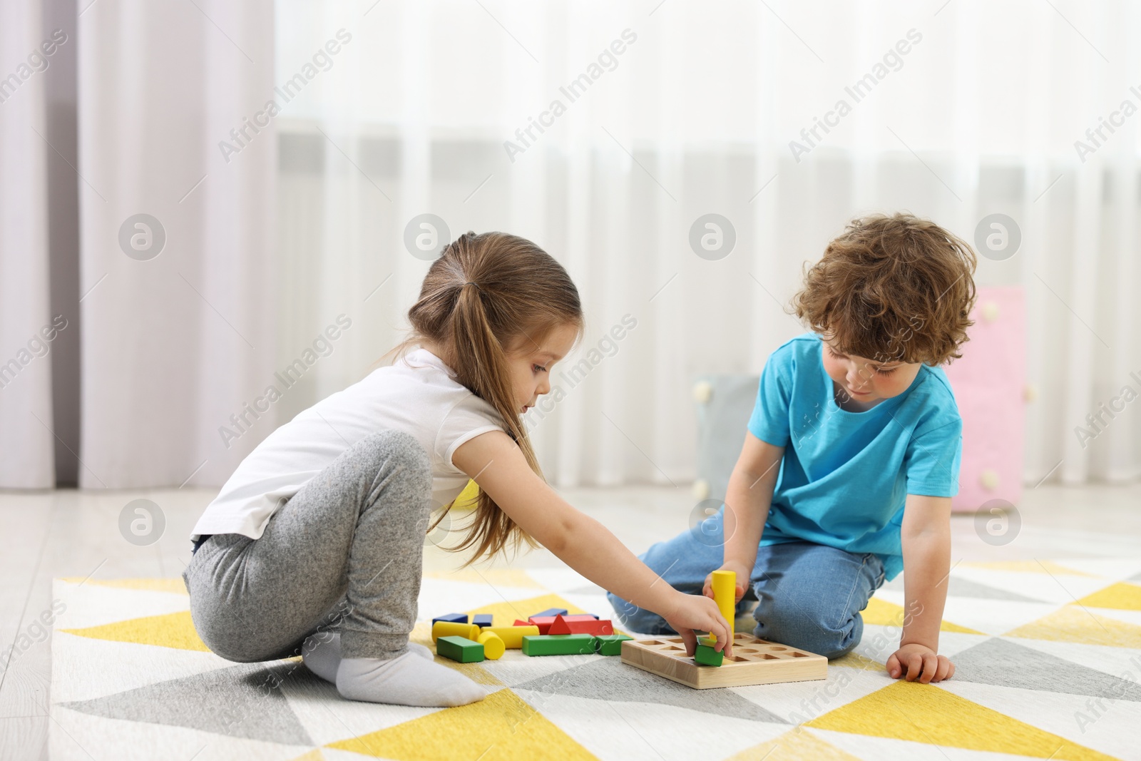 Photo of Cute little children playing with set of wooden geometric figures on floor in kindergarten