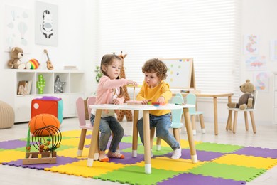 Photo of Cute little children playing with colorful toy pyramid at white table in kindergarten