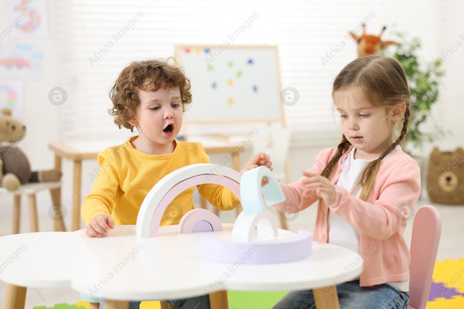 Photo of Cute little children playing with colorful toy rainbow at white table in kindergarten