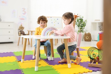 Photo of Cute little children playing with colorful toy rainbow at white table in kindergarten