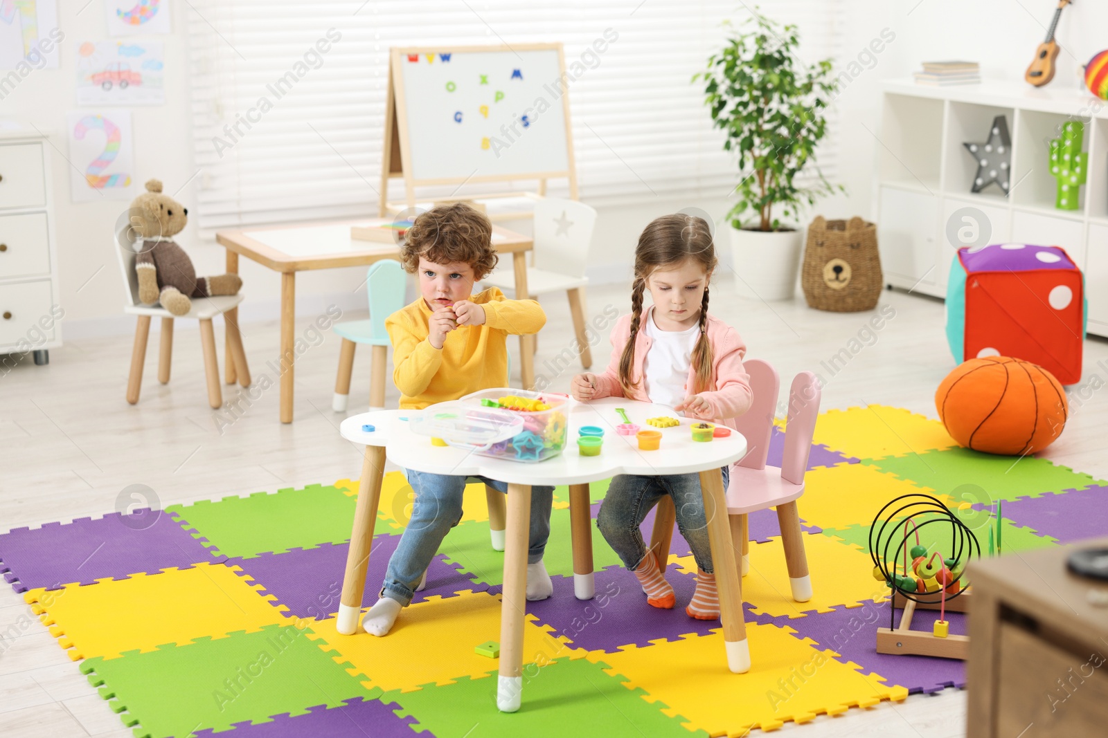 Photo of Cute little children modeling from plasticine at white table in kindergarten