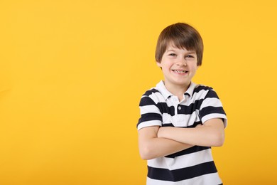 Photo of Portrait of cute little boy with crossed arms on orange background, space for text