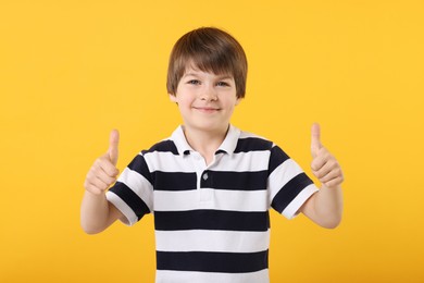Photo of Cute little boy showing thumbs up on orange background
