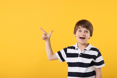 Photo of Cute little boy pointing at something on orange background, space for text
