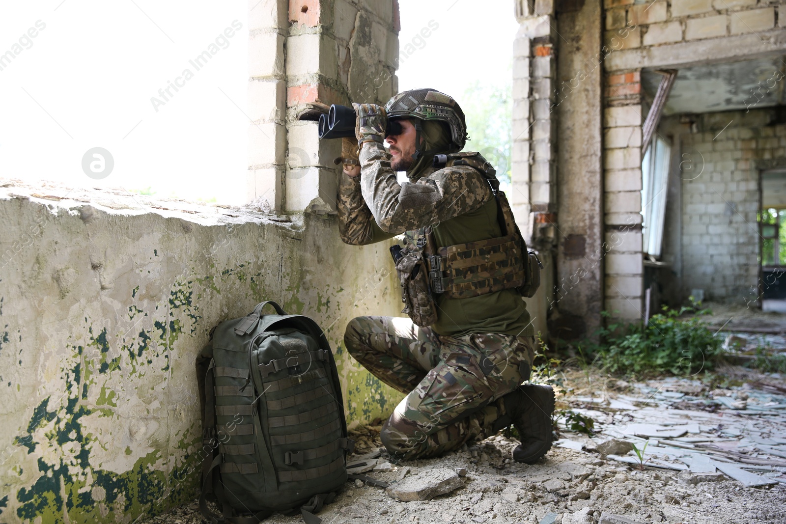 Photo of Military mission. Soldier in uniform with binoculars inside abandoned building