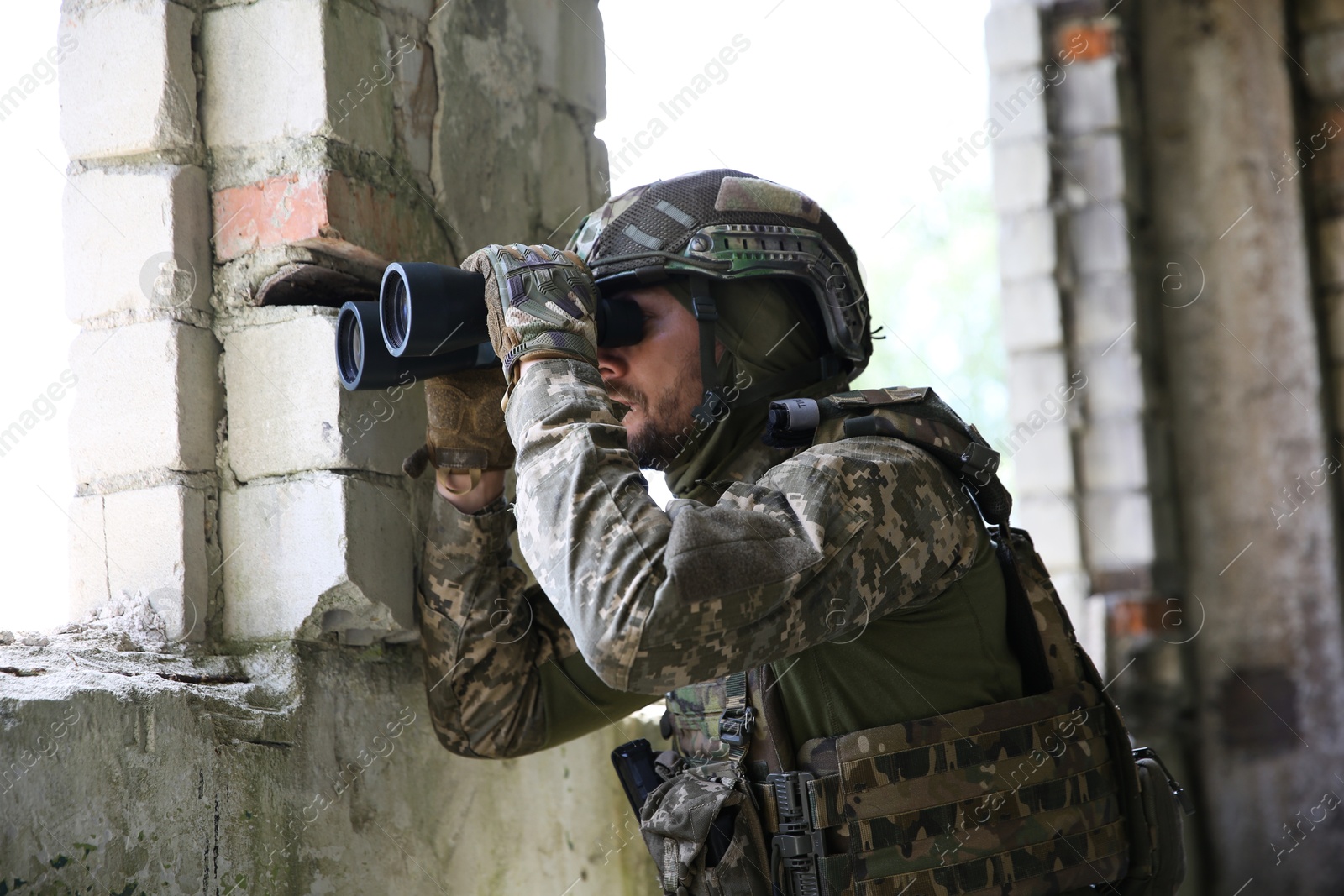 Photo of Military mission. Soldier in uniform with binoculars inside abandoned building