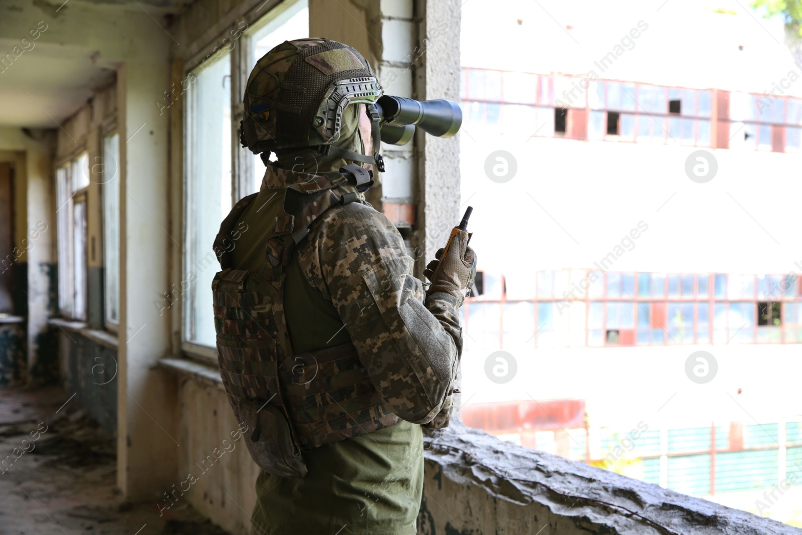 Photo of Military mission. Soldier in uniform with binoculars inside abandoned building, back view. Space for text