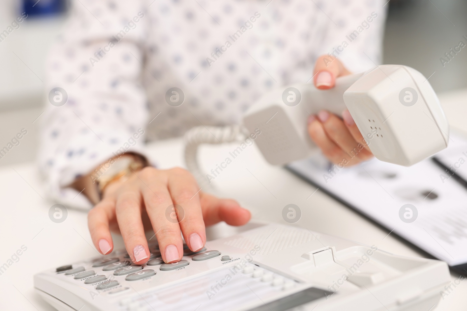 Photo of Secretary dialing number on telephone at table in office, closeup