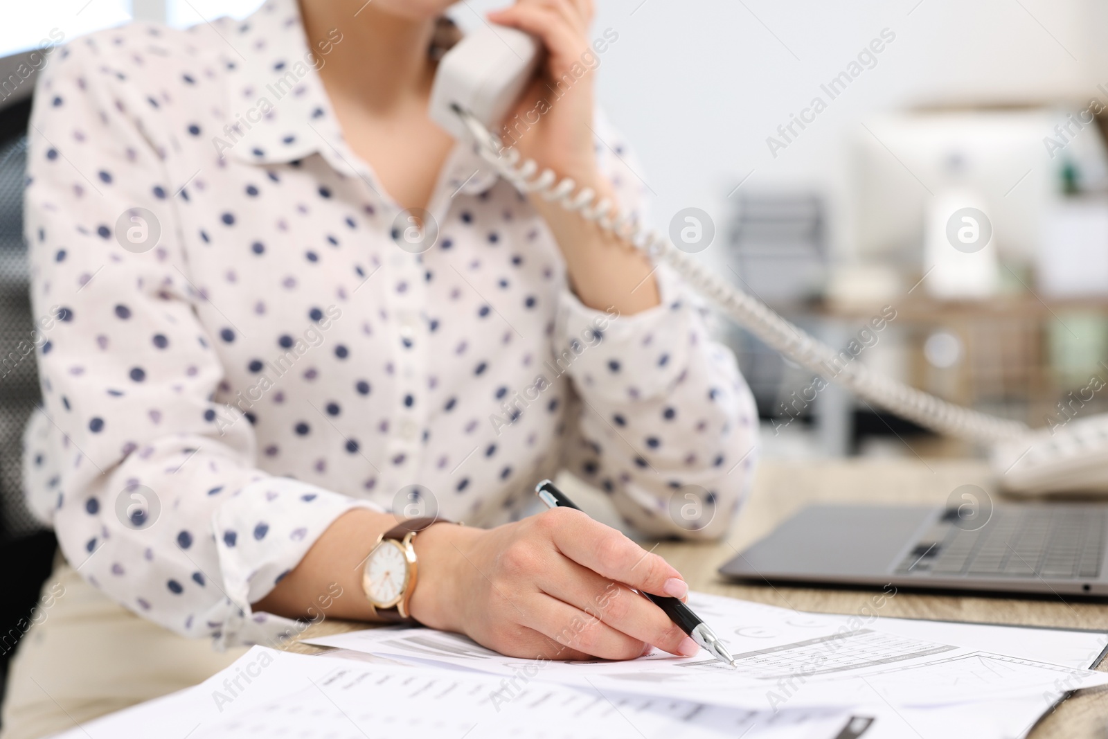 Photo of Secretary talking on telephone at table in office, closeup