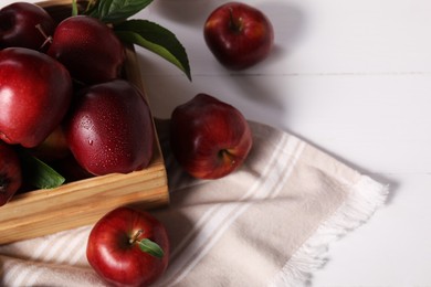 Photo of Fresh red apples with leaves in crate on white wooden table. Space for text