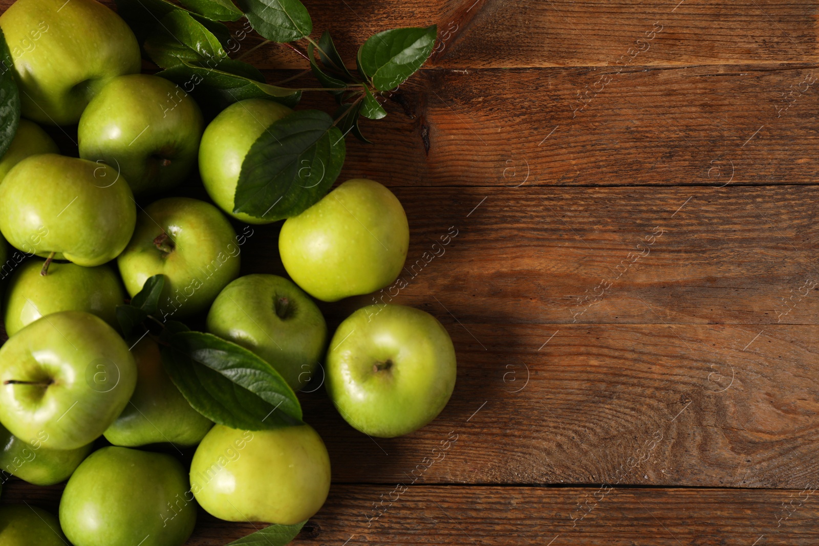 Photo of Ripe green apples with leaves on wooden table, flat lay. Space for text