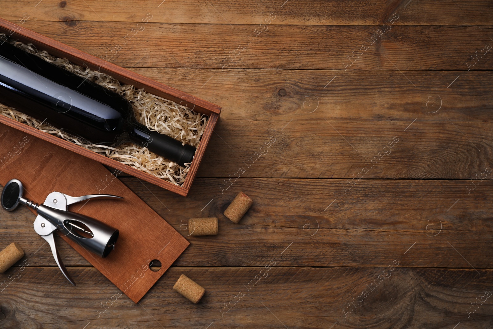 Photo of Box with wine bottle, wing corkscrew and corks on wooden table, flat lay. Space for text