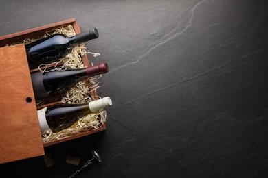 Photo of Box with wine bottles and corkscrew on dark textured table, top view. Space for text