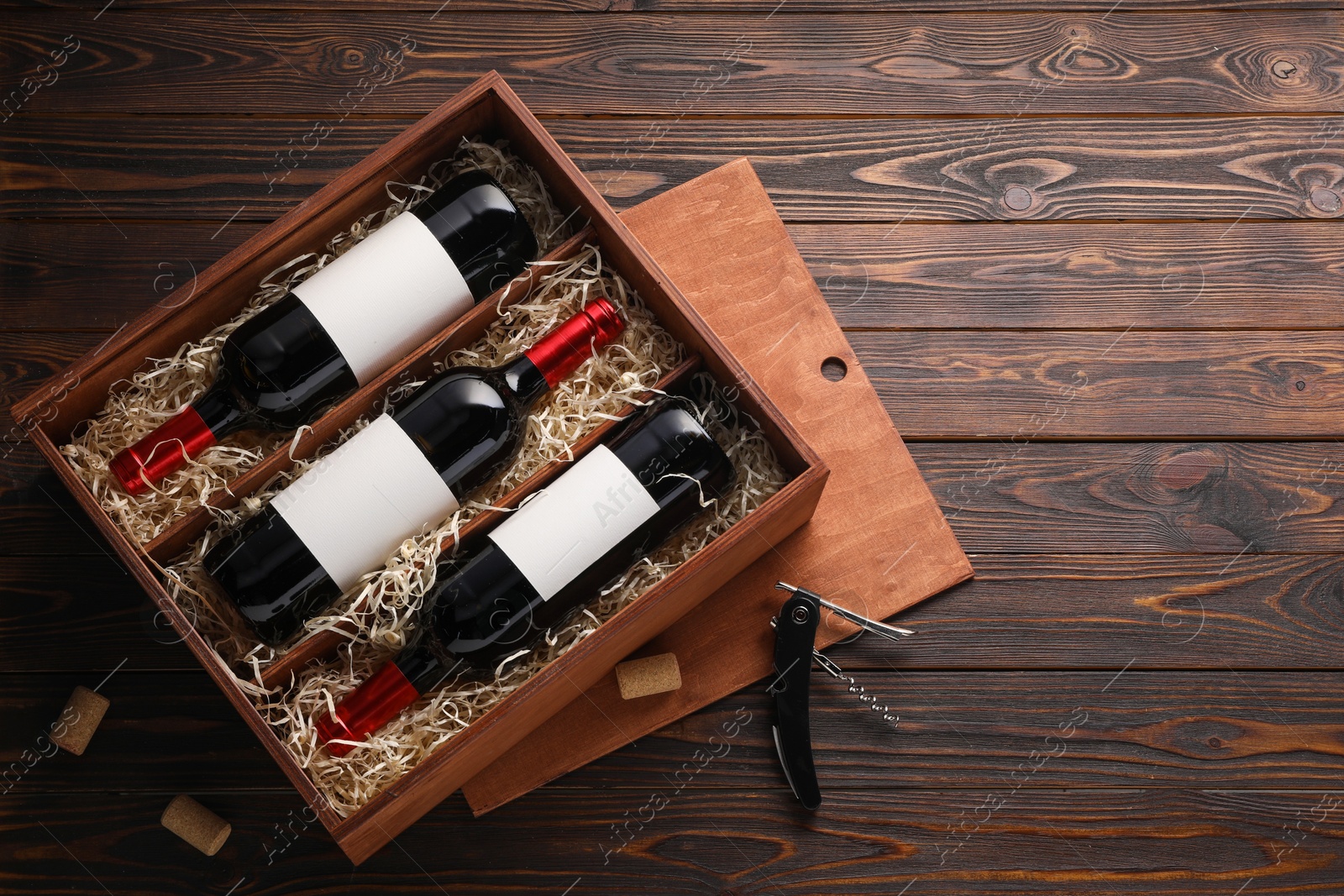 Photo of Box with wine bottles, corkscrew and corks on wooden table, flat lay. Space for text