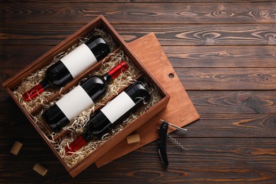 Photo of Box with wine bottles, corkscrew and corks on wooden table, flat lay. Space for text