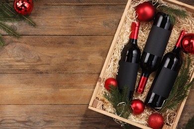 Photo of Wooden crate with bottles of wine, fir twigs and red Christmas balls on table, top view. Space for text