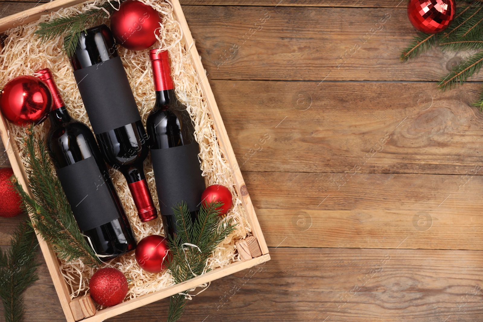 Photo of Wooden crate with bottles of wine, fir twigs and red Christmas balls on table, top view. Space for text