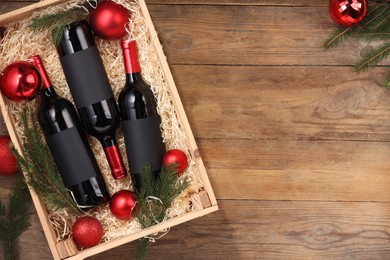 Photo of Wooden crate with bottles of wine, fir twigs and red Christmas balls on table, top view. Space for text