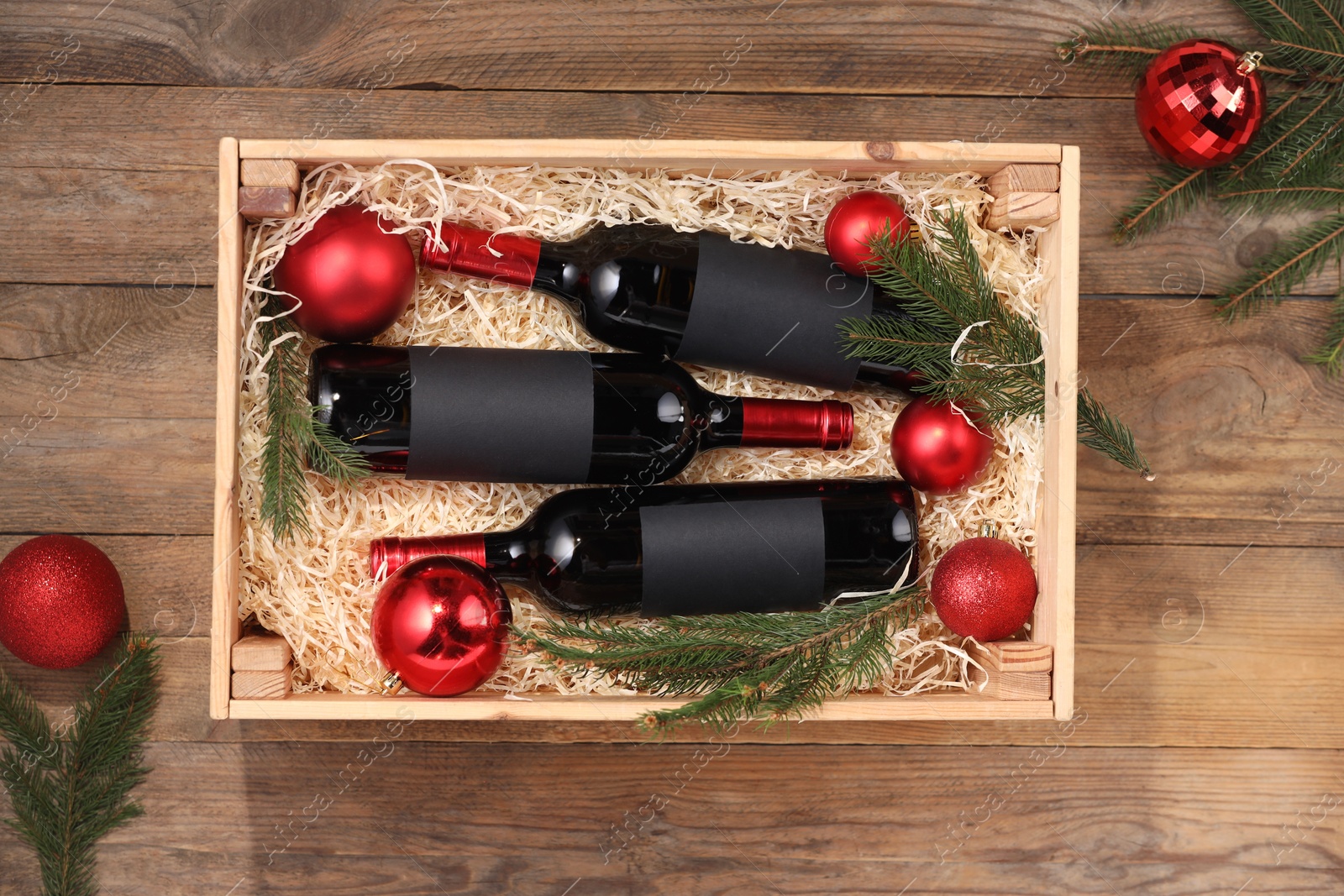 Photo of Wooden crate with bottles of wine, fir twigs and red Christmas balls on table, top view