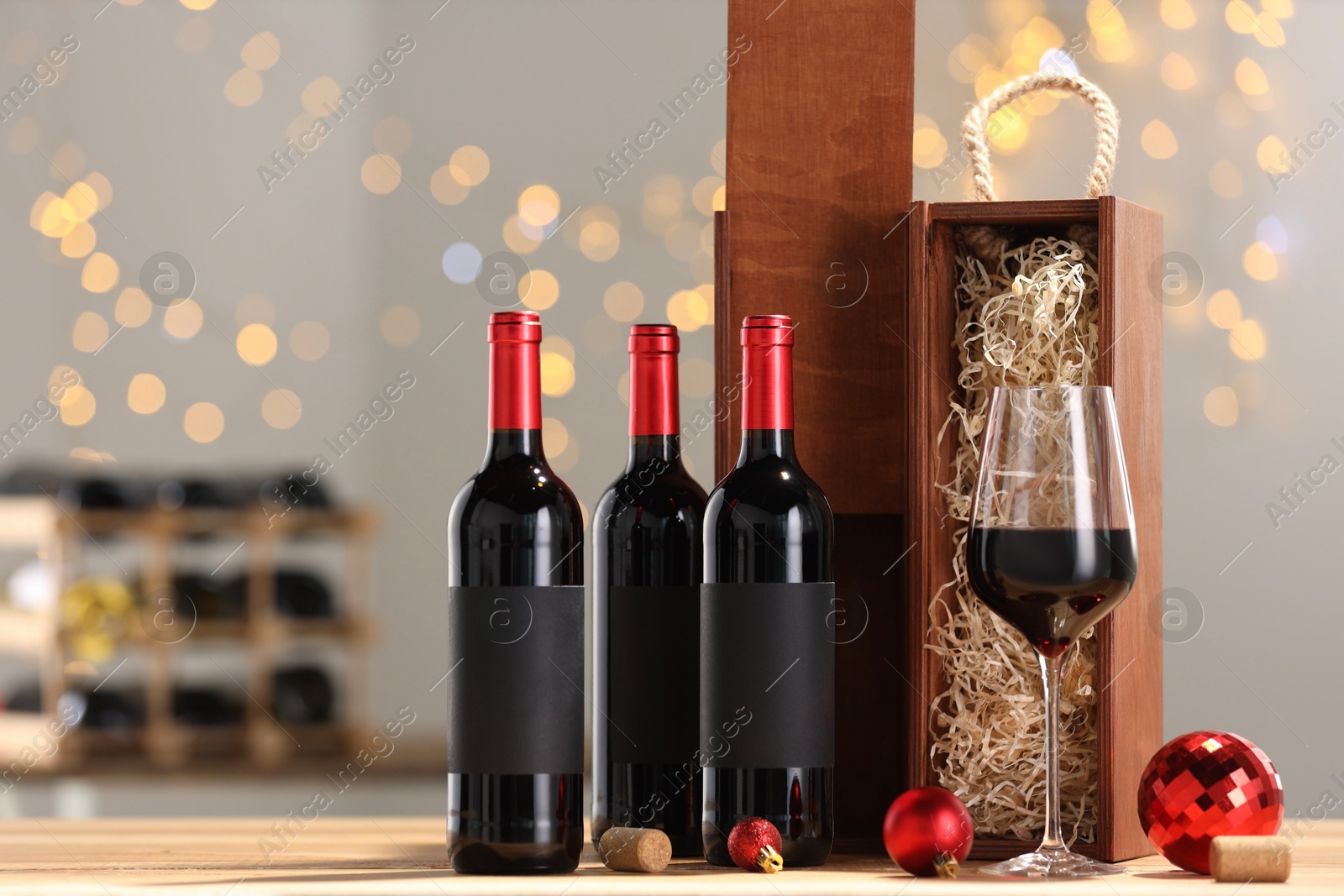 Photo of Bottles of wine, glass, wooden gift boxes, corks and red Christmas balls on table, space for text